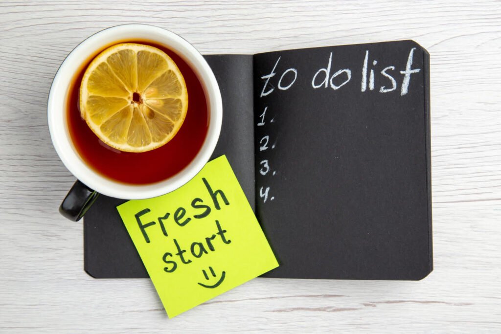 Top view of a dark open notepad, a cup of tea, and motivational notes on a white background, featuring the message 'Fresh start :)'