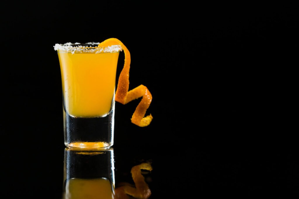 Shot glass filled with orange juice, representing liquid Vitamin C, known for its high bioavailability and purity.